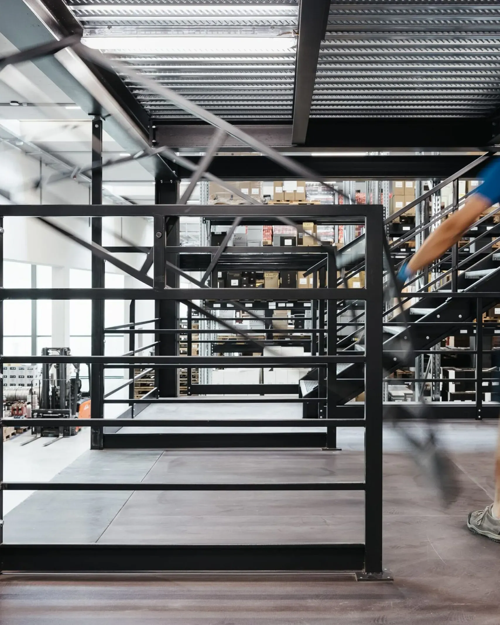 Industriehalle eines Metallbau-Unternehmens in Südtirol; eine Person in Arbeitskleidung geht über eine Stahlgalerie, Geländer und Lager im Hintergrund.